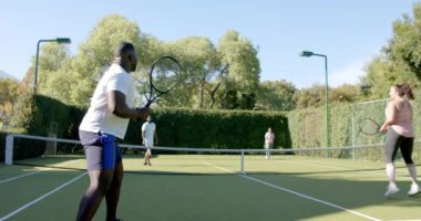 Çiftler tenis oynar, çeşitli arkadaşlar sahada eğlenir, eğlenir. Spor, rekabet, takım çalışması, fitness, eğlence, açık hava