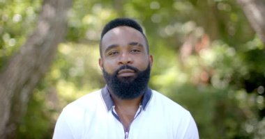 Arka bahçede sakallı, gülümseyen Afrikalı Amerikalı bir adam. Yeşillik ve güneş ışığı dingin bir zemin oluşturuyor. Huzurlu bir atmosfer yaratıyor. Değişmemiş, ağır çekim.