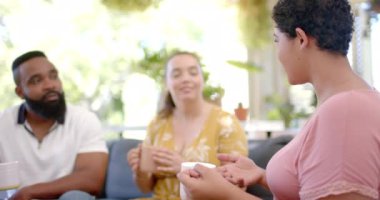 Bir grup arkadaş kanepede oturuyor, kahve içiyor ve sohbet ediyorlar. Arkadaşlık, sosyalleşme, kapalı alan, rahatlama, iletişim, boş zaman, değiştirilmemiş, yavaş çekim