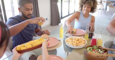 Çeşitli arkadaşlar hamburger, patates kızartması ve salata yiyor, evde birlikte yemeğin tadını çıkarıyorlar. yiyecek
