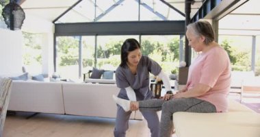 Fizyoterapist, ev ortamında bacak egzersizi yapan yaşlı Asyalı kadına yardım ediyor. Rehabilitasyon, fizyoterapi, sağlık, yardım, iyileşme