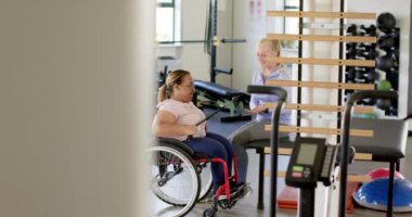 Tekerlekli sandalyede felçli bir kadın rehabilitasyon merkezinde terapistle egzersiz yapıyor. Fizyoterapi, sağlık hizmeti, fitness, egzersiz, terapi, iyileşme, değişmemiş, yavaş çekim