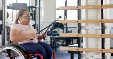 Tekerlekli sandalyede egzersiz yapan, rehabilitasyon için direniş bantlarını kullanan bir kadın, fotokopi alanı. Fitness, adaptif, egzersiz, fizik tedavi, direnç eğitimi, sağlık, değişmemiş, yavaş çekim