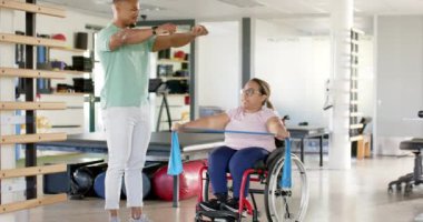 Direniş bandıyla egzersiz, tekerlekli sandalyede felçli bir kadın ve rehabilitasyonda bir terapist. fiziksel terapi, egzersiz, direnç eğitimi, hareketlilik, sağlık hizmetleri, değişmemiş, yavaş çekim