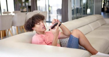 Akıllı telefondan konuşmak, modern oturma odasındaki kanepede dinlenen genç adam. Teknoloji, iletişim, rahatlama, gündelik, ev, yaşam tarzı