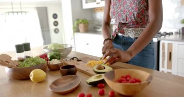 Çiçekli bluz giyen Afro-Amerikalı genç kadın evde, mutfakta sebze kesiyor. Koyu renk saçları, kahverengi gözleri var, ve kolsuz bir bluz giyiyor, değiştirilmemiş, yavaş çekim