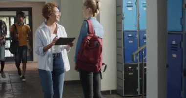 Lisedeyken, sırt çantalı genç bir kız dolapların yanında arkadaşlarıyla gülümsüyor ve konuşuyordu. Eğitim, öğrenciler, arkadaşlık, lise, sohbet, mutluluk
