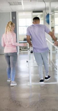 Dikey video: Destekle yürümek, protez bacaklı kadın ve rehabilitasyon merkezinde terapist. Fizyoterapist, fizyoterapi, sağlık, sağlık, iyileşme, protez, yavaş çekim