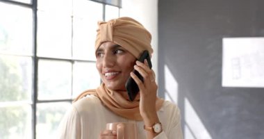 Akıllı telefondan konuşmak, elinde kahve fincanı tutan ve ofis ortamında gülümseyen bir kadın. İş, iletişim, teknoloji, işyeri, profesyonel, çoklu görev