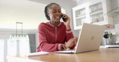 Afro-Amerikalı genç bir kadın telefonda konuşuyor, notlar yazıyor, evde. Koyu renk saçlı, kırmızı kapüşonlu, evde dizüstü bilgisayarı açık, değiştirilmemiş, ağır çekimde.