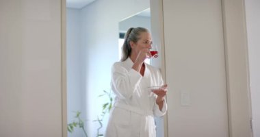 Bornoz giymiş, olgun bir kadın sıcak ev ortamında çay içiyor. Rahatlama, rahatlık, sabah, yaşam tarzı, içecek, değiştirilmemiş, yavaş çekim