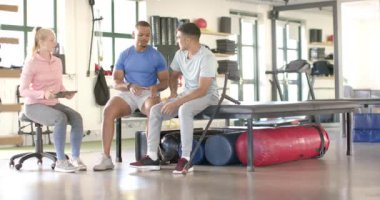 Fizyoterapist, spor salonunda iki adamla rehabilitasyon egzersizlerini tartışıyor. Fizyoterapi, sağlık hizmeti, eğitim, fiziksel eğitim, fitness, takım çalışması, değiştirilmemiş, yavaş çekim