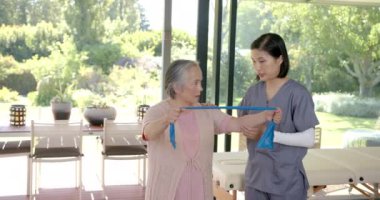 Üst düzey Asyalı kadın evde terapistli direniş bandı kullanıyor. egzersiz, fizyoterapist, fizyoterapi, rehabilitasyon, sağlık hizmetleri, fitness