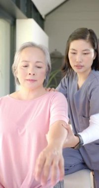 Dikey video: Kol egzersizlerinde yaşlı kadına yardım etmek, evde terapi seansı düzenlemek. Bakım, fizyoterapi, evde bakım, rehabilitasyon, sağlık hizmetleri, yaşlılar