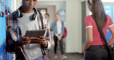 Tablet kullanan bir ergen, lise koridorundaki dolapların yanında arkadaşlarıyla dikiliyor. Eğitim, teknoloji, öğrenci, arkadaşlık, grup, iletişim