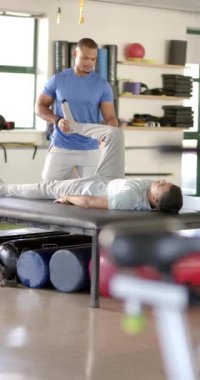 Dikey video: Klinikte rehabilitasyon sırasında hastanın bacağını esneten fizyoterapist. Fizyoterapi, sağlık, tıbbi, terapi, egzersiz, tedavi, yavaş çekim