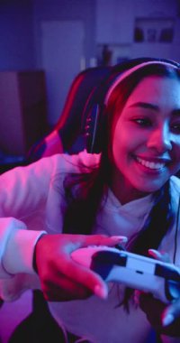 Dikey video: Video oyunları oynamak, kulaklık takan ve oyun sandalyesinde gülümseyen bir kadın. eğlence, teknoloji, esportlar, rahatlama, sanal, aygıt