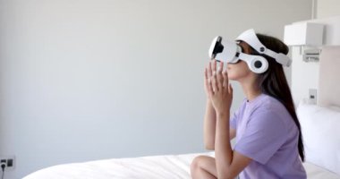 VR kulaklık kullanan, yatakta oturan ve sanal çevreyle etkileşim halinde olan bir kadın, kopyalama alanı. Sanal gerçeklik, teknoloji, etkileşim, sürükleyici, yenilik, fütüristik
