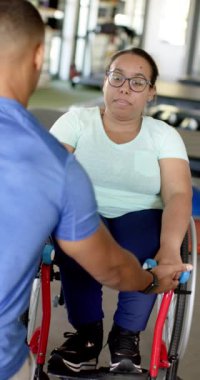 Dikey video: Halterli egzersiz, rehabilitasyon merkezinde terapistin yardımcı olduğu tekerlekli sandalyedeki kadın. Fitness, egzersiz, iyileşme, güç, eğitim, yavaş çekim