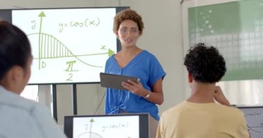 Matematik öğretmeni, tablet kullanan ve lisede öğrencilere grafik açıklayan bir kadın. Eğitim, sınıf, öğrenme, teknoloji, öğretim, akademik