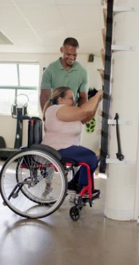 Dikey video: Tekerlekli sandalyedeki kadına yardım etmek, rehabilitasyon egzersizleri sırasında ilerlemeyi teşvik eden terapist. fizyoterapi, sağlık, destek, iyileşme, hareketlilik, teşvik, yavaş çekim