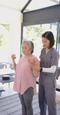 Dikey video: Yaşlı kadına halterlerle yardım etmek, fizik terapist desteği sağlamak. Egzersiz, sağlık, güç, terapi, sağlık, sağlık