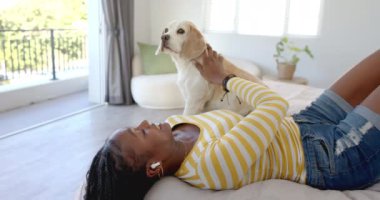 Afro-Amerikalı genç bir kadın evde, evcil bir köpek gibi yatakta uzanıyor. Uzun siyah saçları, sarı çizgili gömleği ve kotu var. Değiştirilmemiş, ağır çekimde.