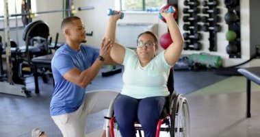 Fizyoterapist, tekerlekli sandalyede belden aşağısı felçli bir kadına yardımcı oluyor. Spor salonunda halterleri kaldırıyor. Rehabilitasyon, fizyoterapi, sağlık, fitness, egzersiz, dayanıklılık eğitimi, değişmemiş, yavaş çekim