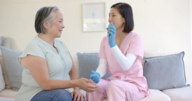 Pembe önlüklü hemşire evde fizik tedavi gören yaşlı Asyalı kadına yardım ediyor. Sağlık, kıdemli bakım, rehabilitasyon, fizyoterapi, yardım, evde bakım