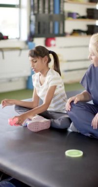 Dikey video: Engelli rehabilitasyonunda, terapist ile otururken kız oyuncakla oynuyor. Fizyoterapi, rehabilitasyon, sağlık, mesleki terapi, çocuk, tedavi