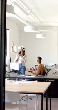 Dikey video: VR kulaklık kullanan kadın, meslektaşı modern ofiste gözlemlerken etkileşim içinde. Teknoloji, sanal gerçeklik, yenilik, takım çalışması, işbirliği, profesyonel
