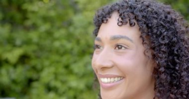 Kıvırcık saçlı, gülümseyen kadın bahçe ortamında eğleniyor. Doğa, rahatlama, yaz mevsimi, mutluluk, yaşam tarzı, rahatlık