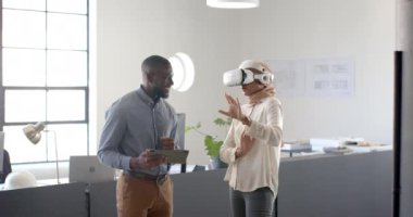 VR kulaklığı kullanan bir kadın, meslektaşı ile iş yerinde tablet tutarken projeyi tartışıyor. Teknoloji, takım çalışması, işbirliği, yenilik, iş yeri, işyeri