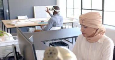 Bilgisayarda çalışan, tesettürlü bir kadın, ofiste kulaklıkları olan bir iş arkadaşı. İş, iş birliği, teknoloji, takım çalışması, işbirliği