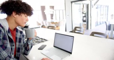 Kahve içmek, modern mutfakta dizüstü bilgisayar ve akıllı telefon kullanmak. Teknoloji, uzaktan çalışma, ev ofisi, üretkenlik, çoklu görev, modern yaşam tarzı