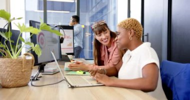 Projede işbirliği yapan iki kadın, ofiste dizüstü bilgisayar ve bilgisayar kullanıyor. Takım çalışması, işbirliği, teknoloji, iş dünyası, profesyoneller, iş arkadaşları