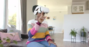 Sanal gerçeklik kulaklığı takan, evdeki, evdeki koltukta oturan, fotokopi çeken Afro-Amerikalı genç bir kadın. Siyah örgülü saçları, renkli süveteri sanal dünyayı keşfediyor, değişmemiş, yavaş çekim