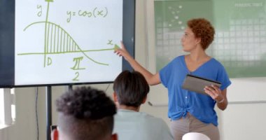 Matematik öğretmeni, elinde tablet olan ve lisede beyaz tahtayı gösteren bir kadın. Eğitim, teknoloji, öğretim, öğrenciler, öğrenme, akademik