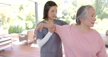 Fizyoterapist, evde kol egzersizleri yapan yaşlı Asyalı kadına yardım ediyor. Rehabilitasyon, yaşlılar, sağlık hizmetleri, terapi, sağlık hizmetleri, bakıcı