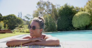 Havuzda dinlenen, güneş gözlüğü takan, gergin, güneşli günün tadını çıkaran, fotokopi çeken bir kadın. Yaz, dinlenme, dinlenme, tatil, güneşlenme, tatil
