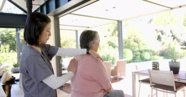 Omuz egzersizlerinde yardımcı olmak, fizyoterapist evde yaşlı Asyalı kadınlara yardım etmek. Fizyoterapi, rehabilitasyon, sağlık hizmetleri, yaşlılar, yardım, tıbbi yardım