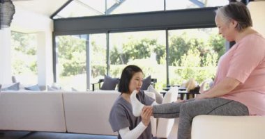 Fizyoterapist, parlak oturma odasında bacak egzersizleri yapan yaşlı Asyalı kadına yardım ediyor. Fizyoterapi, rehabilitasyon, sağlık hizmetleri, yaşlılar, destek, sağlık