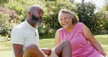 Gülümseyen kıdemli arkadaşlar çimlerin üzerinde oturuyor, parkta sohbetin tadını çıkarıyorlar. Arkadaşlık, açık hava, eğlence, mutluluk, rahatlama, kaynaşma