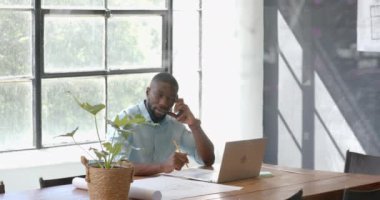 Akıllı telefondan konuşan, dizüstü bilgisayarda çalışan ve ofiste notlar alan bir adam. İş, teknoloji, çoklu görev, üretkenlik, profesyonel, iletişim