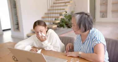 Laptop kullanan rahatlatıcı bir kız, evde ona destek olan Asyalı bir büyükanne. Aile, nesiller arası, teknoloji, bağlanma, teşvik, bağlantı