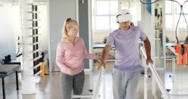 Protez bacaklı bir adam paralel barlarda terapistli VR kulaklık kullanıyor. Fizyoterapist, fizyoterapi, rehabilitasyon, sağlık, tıbbi, teknoloji, değişmemiş, yavaş çekim