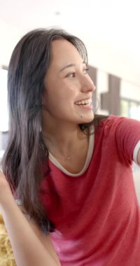 Dikey video: Kırmızı tişörtlü gülümseyen kadın arkadaşlarıyla evde takılırken eğleniyor. Arkadaşlık, mutluluk, birliktelik, eğlence, sosyalleşme, eğlence.