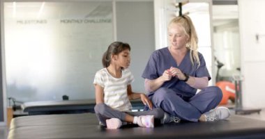 Ameliyat önlüklü bir fizyoterapist, rehabilitasyon seansında beyin felci geçiren genç bir kıza yardım ediyor. Fizyoterapi, rehabilitasyon, sağlık, destek, yardım, iyileşme, değişmemiş, yavaş çekim