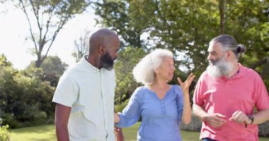 Kıdemli arkadaşlar parkta yürüyüp konuşuyorlar, güneşli günün tadını çıkarıyorlar. Arkadaşlık, açık hava, eğlence, doğa, arkadaşlık, sohbet.