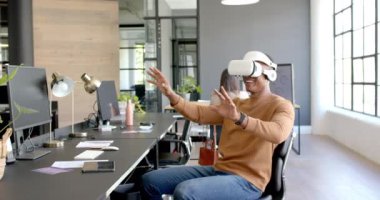 Afro-Amerikan bir adam modern ofiste masasında oturmuş gülümsüyor ve iletişim kuruyor. Teknoloji, sanal gerçeklik, iş, etkileşim, çalışan, çalışma alanı